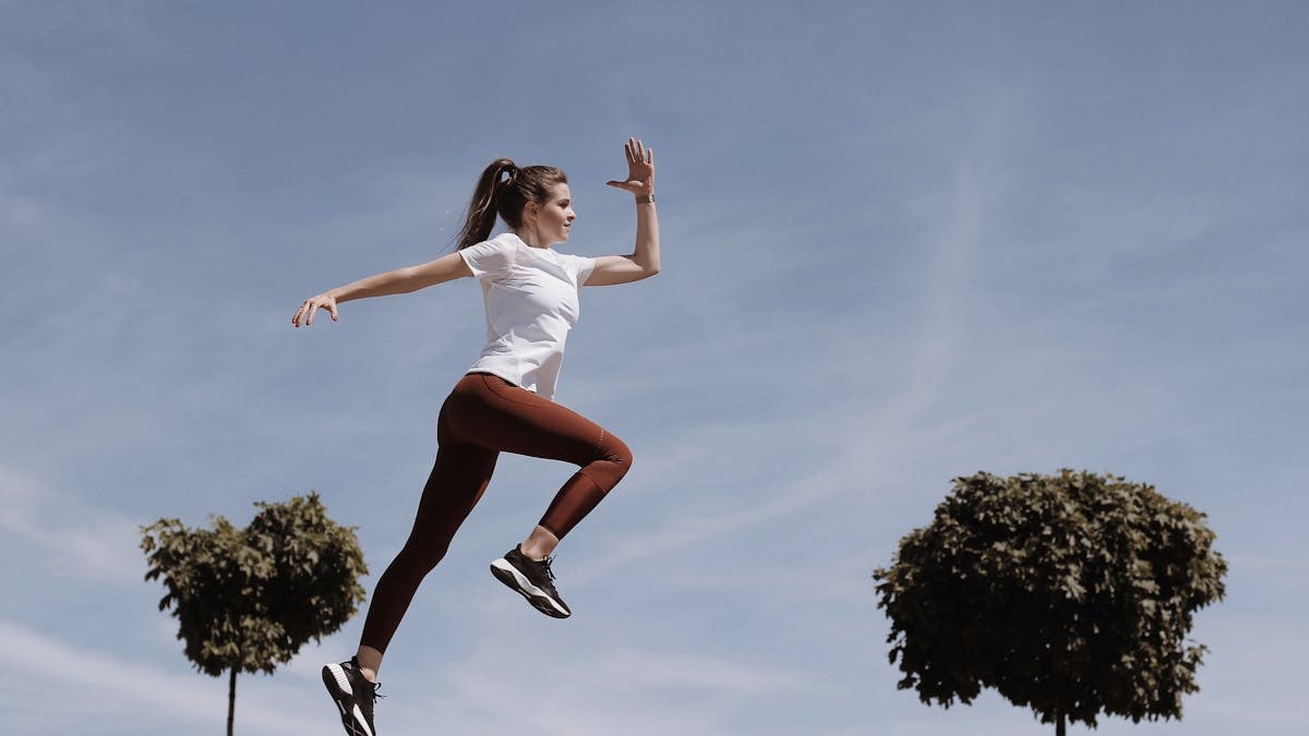 Athletic woman in action jump against a blue sky background. Captures fitness in motion.